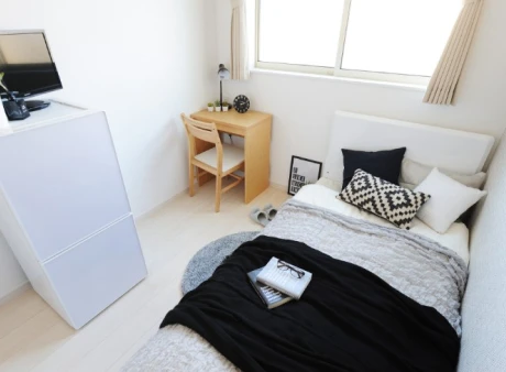 A room with a bed, refrigerator and desk